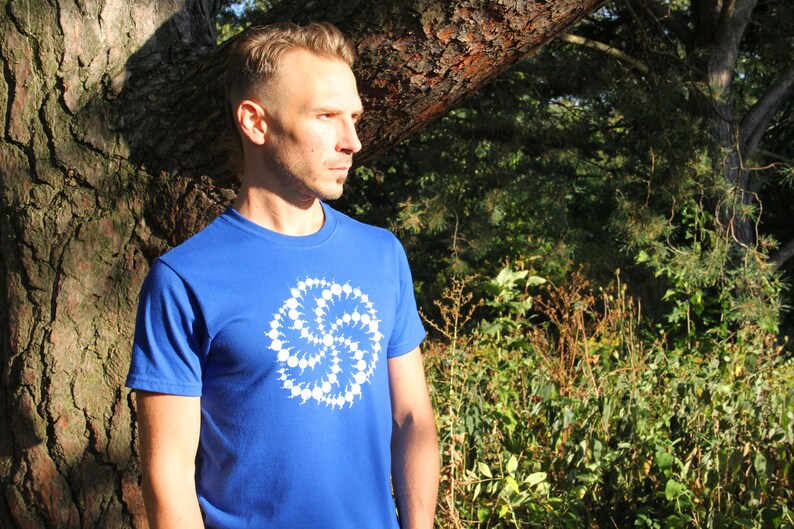 Puede incluir: Un hombre lleva una camiseta azul real con un dise&ntilde;o geom&eacute;trico blanco. El dise&ntilde;o es un patr&oacute;n circular de puntos y l&iacute;neas blancas.
