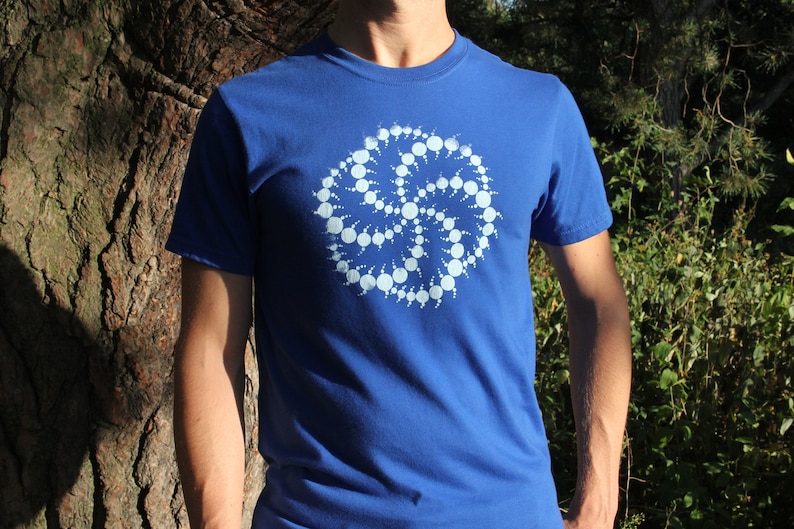 Puede incluir: Una camiseta azul real con un dise&ntilde;o geom&eacute;trico blanco en forma de espiral.