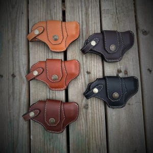 May include: Five leather holsters in different colors and styles. The holsters are made of brown and black leather and have a stitched design.
