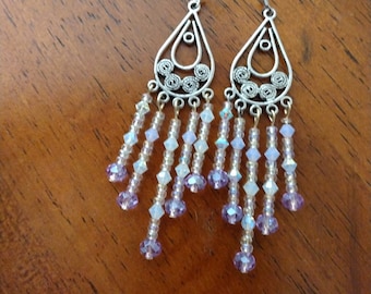 May include: Silver dangle earrings with a teardrop-shaped design and a beaded fringe. The beads are a mix of clear and light purple.