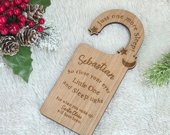 May include: A light brown wooden door hanger with the engraved text: Just one more sleep! Sebastian, so close your eyes Little One and Sleep tight, For when you wake up Santa Claus will have been. The hanger features star and moon cutouts.