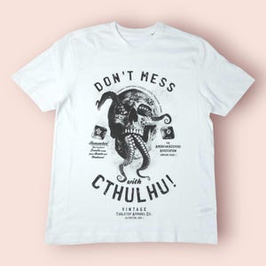 May include: White t-shirt with a black graphic featuring a skull with tentacles and the text "DON'T MESS with CTHULHU!". Additional text includes "Vintage Tabletop Apparel Co." and "The American Keepers Association".