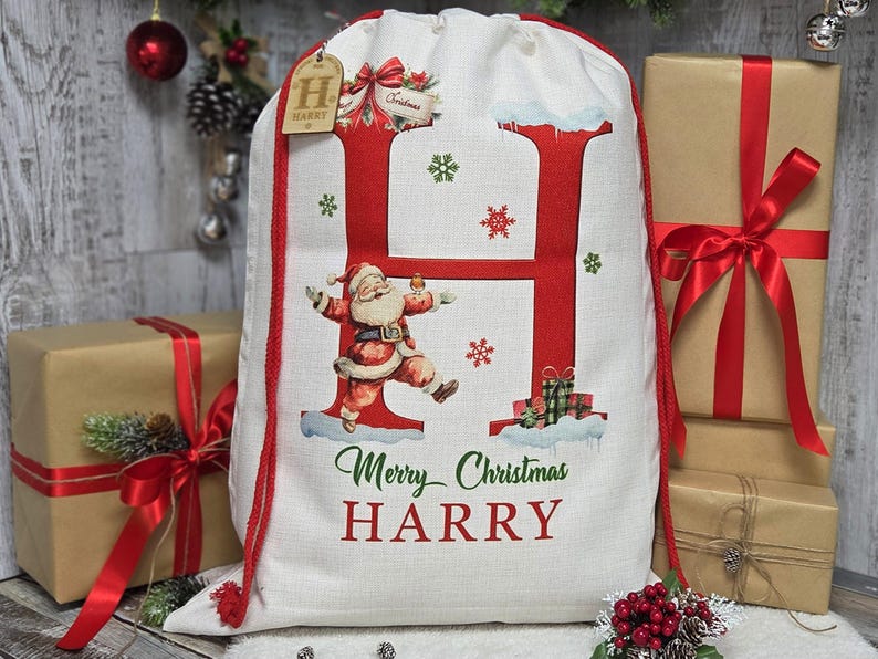 May include: A white Christmas gift bag with a large red letter "H" and a Santa Claus illustration. The bag has a red drawstring and the words "Merry Christmas HARRY". Presents wrapped in brown paper with red ribbons are in the background.