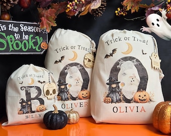 May include: Halloween-themed drawstring bags with "Trick or Treat" text, bats, and a crescent moon design. The bags feature illustrations of a witch, a pumpkin, and a ghost. The names "Billy", "Oliver", and "Olivia" are printed on the bags. A sign reads "Tis the Season to be Spooky".