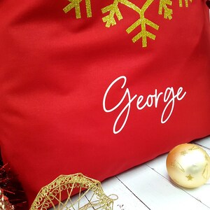 May include: Red fabric gift bag with a gold snowflake design and the name "George" printed in white.