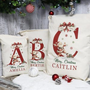 May include: Off-white Christmas sacks with red letters A, B, and C, each featuring a Santa Claus illustration and the words "Merry Christmas." The sacks are personalized with names and decorated with snowflakes and bows.