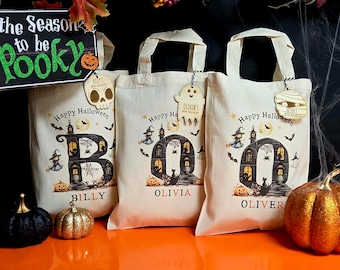 May include: Three Halloween-themed tote bags with personalized names and spooky illustrations. Each bag features a haunted house design, bats, and the words "Happy Halloween." Decorative pumpkins and a sign that says "the Season to be Spooky" complete the festive scene.