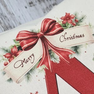 May include: Close-up of a Christmas-themed design featuring a large red bow with white stripes, and the words "Merry Christmas" on a banner. The design includes red poinsettias and green foliage on a cream-colored background.
