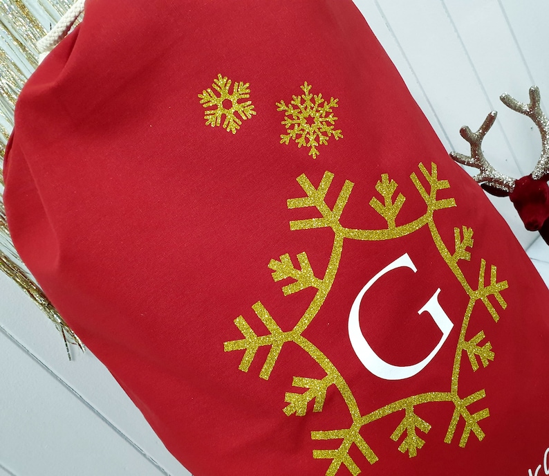 May include: Red Christmas gift bag with a gold snowflake design and the letter "G" in white.