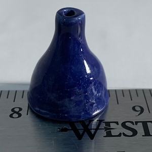 Op de afbeelding: Een kleine, donkerblauwe keramische flesstopper met een ronde bovenkant en een klein gaatje in het midden. De stopper is ongeveer 2,5 cm hoog en ligt op een liniaal.