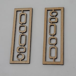 May include: Two rectangular light brown wooden cutouts featuring an open frame design. Each piece contains a vertical arrangement of interconnected rounded rectangular shapes within the outer border, creating a geometric pattern with negative space.