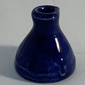 Op de afbeelding: Een kleine, donkerblauwe keramische vaas met een witte glazuur. De vaas heeft een ronde, bolle vorm en een smalle opening aan de bovenkant.