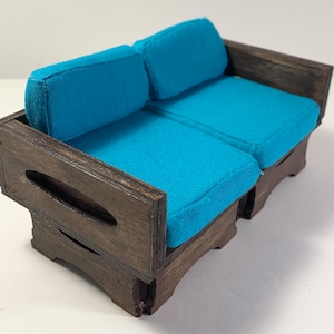 May include: A miniature wooden couch with a teal blue fabric cushion. The couch has a dark wood stain and a simple design.