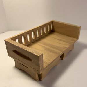 May include: A wooden tray painted in a light brown color. The tray has a rectangular shape with a raised back featuring several oval cutouts. The sides have curved cutouts for handles, and the base has decorative feet.