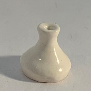 Op de afbeelding: Een kleine, witte keramische vaas met een ronde basis en een smalle hals.