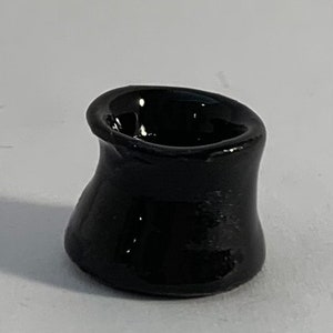 Op de afbeelding: Een kleine, zwarte keramische pot met een afgeronde, licht uitlopende opening. De pot heeft een gladde, glanzende afwerking.