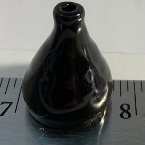 Op de afbeelding: Een kleine, zwarte keramische vaas met een ronde basis en een smalle opening aan de bovenkant. De vaas is ongeveer 2,5 cm hoog.