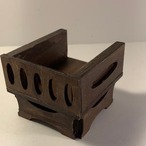 May include: A dark brown wooden box with a rectangular shape. The box has a series of oval cutouts on the sides and decorative curved cutouts. The box is designed to hold small items.
