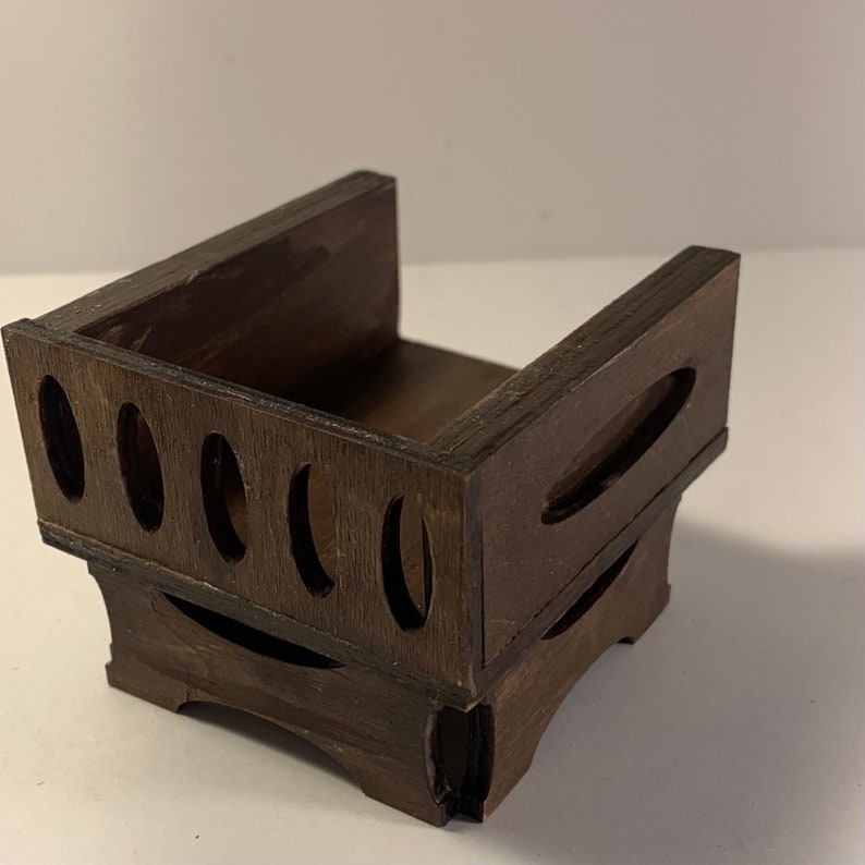 May include: A dark brown wooden box with a rectangular shape. The box has a series of oval cutouts on the sides and decorative curved cutouts. The box is designed to hold small items.