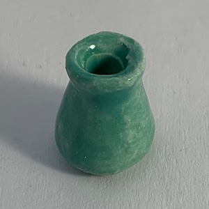 Op de afbeelding: Een kleine, turquoise keramische vaas met een afgeronde body en een brede, licht uitlopende opening. De vaas heeft een getextureerd oppervlak en een gladde, glanzende afwerking. De vorm doet denken aan een kleine buidel.