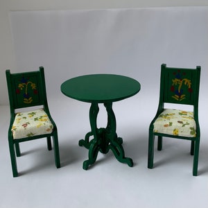 May include: A green table and two chairs with floral patterned cushions. The table has a round top and four legs. The chairs have a high back and are painted green with floral designs.