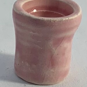 Op de afbeelding: Een kleine, roze keramische plantenpot met een glad, licht getextureerd oppervlak. De pot heeft een brede opening en een afgeronde bodem.