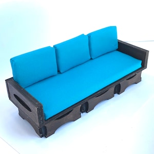 May include: A miniature wooden sofa with a blue fabric cushion and three pillows. The sofa has a dark wood finish and a simple design.