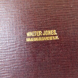 May include: Close-up of a dark red leather surface with gold lettering that reads "WALTER JONES. 195 & 196 GLOANE ST. S.W."
