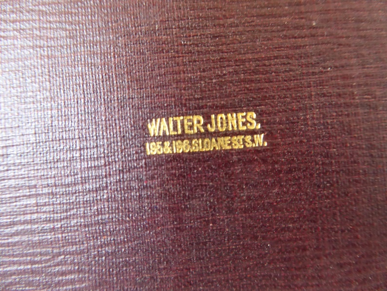 May include: Close-up of a dark red leather surface with gold lettering that reads "WALTER JONES. 195 & 196 GLOANE ST. S.W."