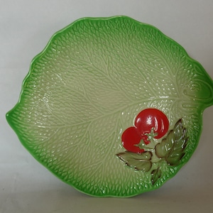 May include: A green ceramic leaf-shaped serving dish with a raised design of a vine with two red tomatoes.