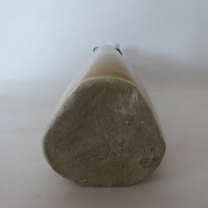 May include: A close-up of the bottom of a stoneware bottle. The bottle is a light brown color and has a textured surface.