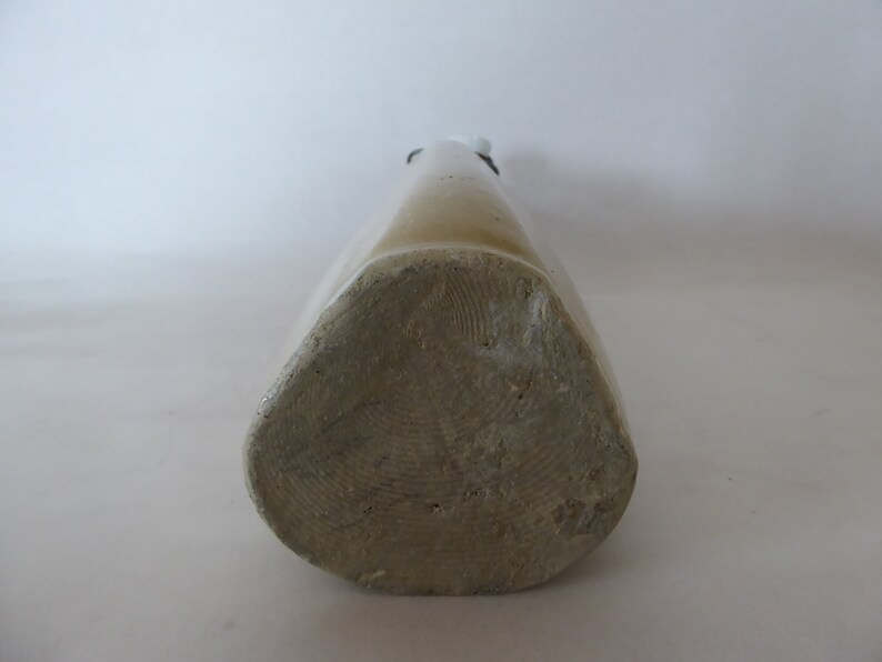 May include: A close-up of the bottom of a stoneware bottle. The bottle is a light brown color and has a textured surface.