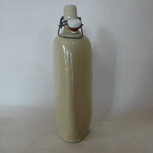May include: A ceramic bottle with a metal swing top lid. The bottle is a light beige color and has a slightly textured surface.