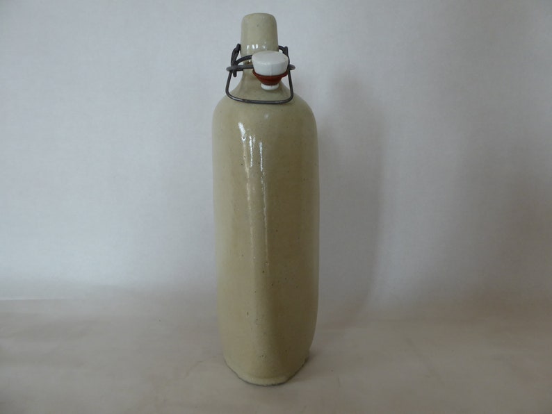 May include: A ceramic bottle with a metal swing top lid. The bottle is a light beige color and has a slightly textured surface.