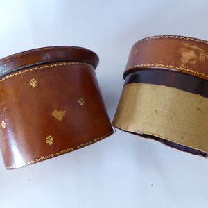 May include: Two brown leather boxes with gold trim and a decorative pattern. The boxes are empty and have a cardboard lining.