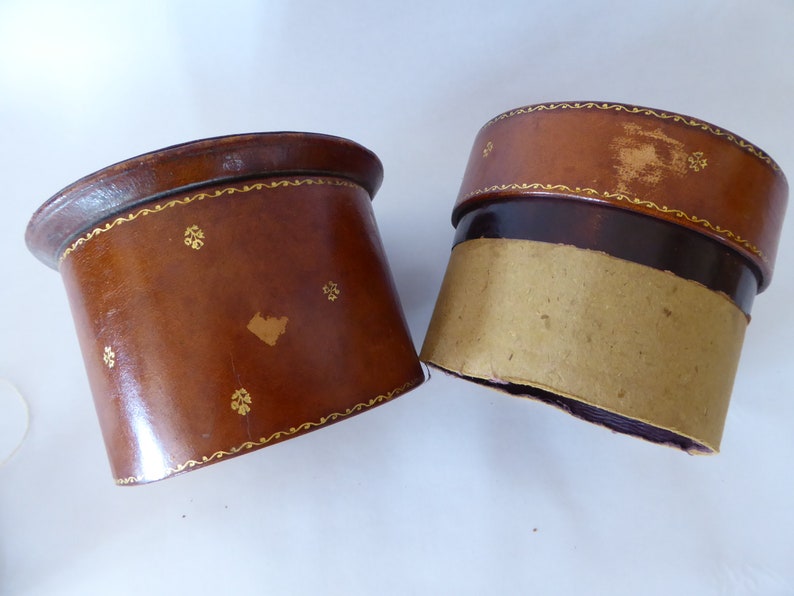 May include: Two brown leather boxes with gold trim and a decorative pattern. The boxes are empty and have a cardboard lining.