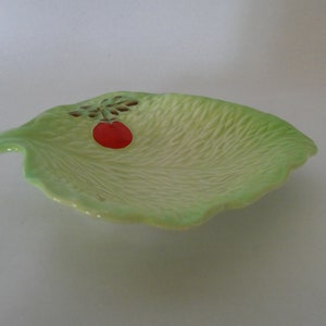 Puede incluir: Un plato de cerámica verde en forma de hoja con una cereza roja pintada.