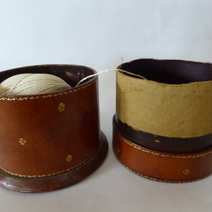 May include: Two brown leather boxes with gold trim. One box has a ball of white string inside. The other box is empty.