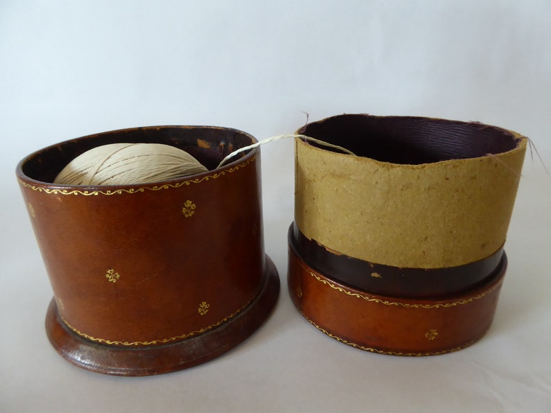 May include: Two brown leather boxes with gold trim. One box has a ball of white string inside. The other box is empty.