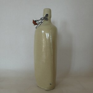 May include: A ceramic bottle with a cream-colored glaze and a metal swing top lid.