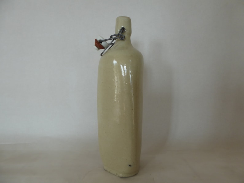 May include: A ceramic bottle with a cream-colored glaze and a metal swing top lid.