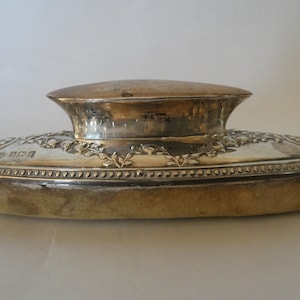 May include: An oval silver box with a hinged lid and a decorative floral design. The box has a soft, beige lining and a beaded border.