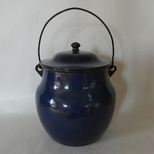 May include: A blue enameled pot with a lid and a wire handle. The pot has a rounded body and a slightly flared rim.