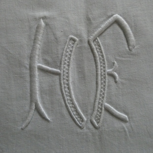 Könnte beinhalten: Weiße gestickte Initialen "AF" auf einem weißen Leinenstoff.