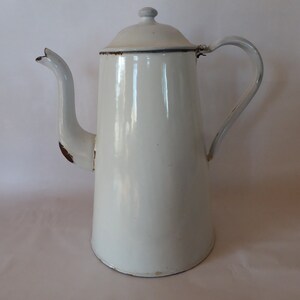 Könnte beinhalten: Weiße Emaille-Kaffeekanne mit abgebrochenem Ausguss und Henkel. Die Kanne hat einen leicht abgenutzten Look.