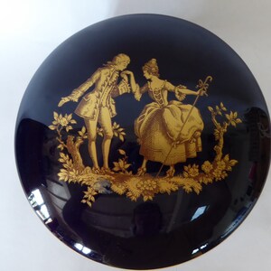 May include: A round, cobalt blue porcelain trinket box with a gold-gilded design of a couple in a garden setting.