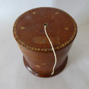 May include: A brown leather box with gold detailing and a white string coming out of the top.