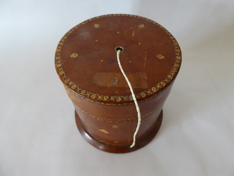 May include: A brown leather box with gold detailing and a white string coming out of the top.