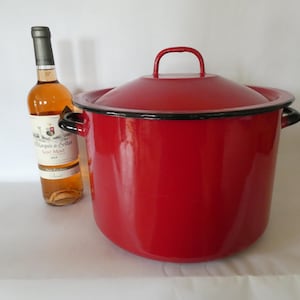 Op de afbeelding: Een grote, cilindrische rode emaille soeppan met bijpassend deksel, voorzien van zwarte randen en twee handgrepen aan de zijkant. Naast de pan staat een glazen fles Marquis de Seillas Saint-Mese roséwijn met een wit etiket en zilveren dop.