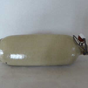 May include: A light beige ceramic bottle with a wire and ceramic stopper. The bottle has a rounded body and a narrow neck.